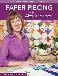 a woman sitting at a table in front of some quilts and potted plants