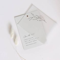 the wedding stationery is laid out on top of an envelope and some white feathers