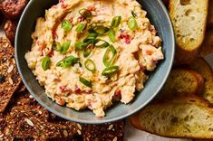 a bowl filled with dip surrounded by bread and crackers on a table top next to other foods