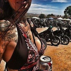 a woman standing in front of a bunch of motorcycles holding a can of beer and looking at the camera