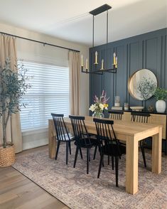 a dining room table with black chairs next to a large mirror and potted plant