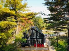 a cabin nestled in the woods with lots of trees around it and red chairs on the porch