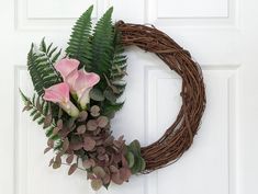 a wreath with pink flowers and greenery hangs on a door