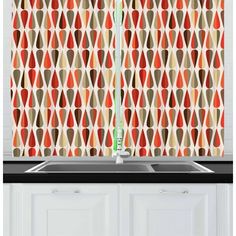 a kitchen curtain with an orange and brown geometric pattern on it, in front of a white cabinet