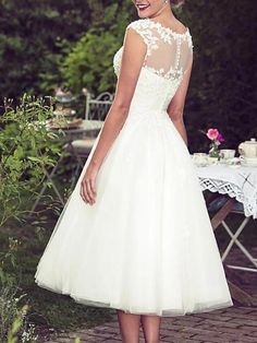 a woman wearing a white dress standing in front of a table with flowers on it