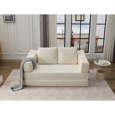 a white couch sitting on top of a rug in a living room next to a window