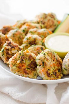 a white plate topped with crab cakes next to a bowl of ranch dressing and an avocado