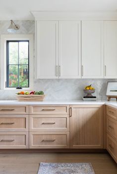 a bowl of fruit sits on the counter in this kitchen with white cabinets and marble backsplash