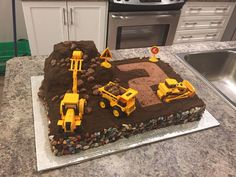 a birthday cake with construction vehicles on it and rocks in the middle, sitting on a kitchen counter