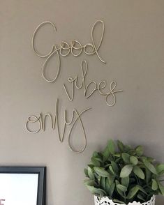 the words good vibe only are spelled in cursive writing on a wall next to a potted plant