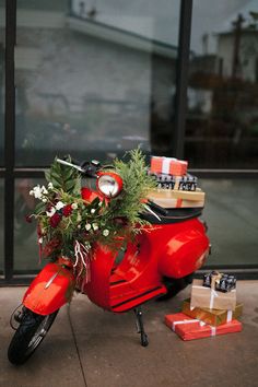 a red scooter parked on the sidewalk with christmas presents in front of it