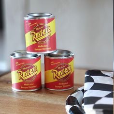 three cans of food sitting on top of a wooden table next to a black and white checkered napkin