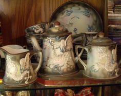 an assortment of antique china on display in a glass case with other items behind it