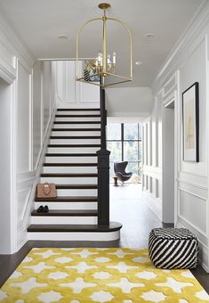 a yellow and white rug on the floor in front of stairs with chandelier