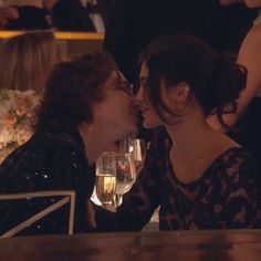 two women sitting at a table kissing each other with wine glasses in front of them