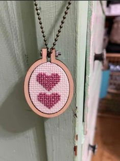 a cross stitch necklace with two hearts hanging from it's front door frame on a chain