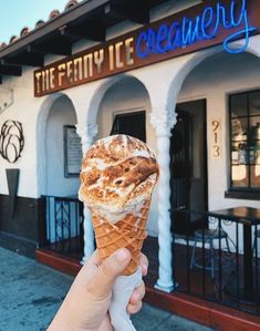 a hand holding an ice cream cone in front of a building