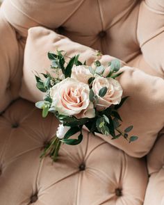 a bouquet of pink roses sitting on top of a beige velvet chair with greenery