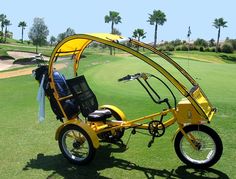 a yellow three wheeled bike parked on top of a grass covered golf course with palm trees in the background