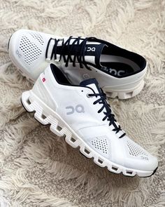 two pairs of white and black running shoes on carpeted area with rug in background