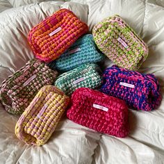 six colorful bags sitting on top of a white bed next to each other in a pile