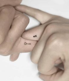 two hands holding each other with small tattoos on their thumbnails and one has an arrow in the middle