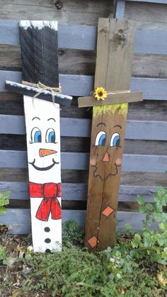 two wooden snowmen standing next to each other in front of a fence with grass