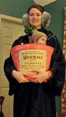 a woman holding a baby in her arms and wearing a fake mandrake costume