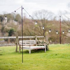 a wooden bench sitting in the middle of a lush green field with string lights hanging from it's poles