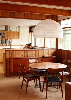 a dining room table and chairs in front of a kitchen with wood paneled walls