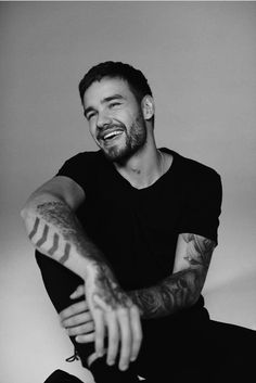 a black and white photo of a man with tattoos on his arm smiling at the camera