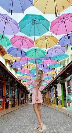 a woman is standing under many umbrellas in an alleyway with shops on both sides