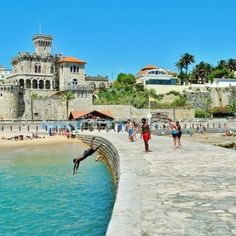 people are walking along the water near an old castle