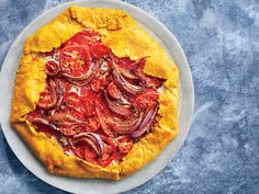 a pizza topped with onions and tomatoes on top of a white plate next to a fork