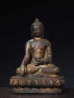 an antique buddha statue sitting on top of a wooden table in front of a black background