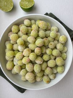 a white bowl filled with sugar covered nuts next to limes and a cloth on the table