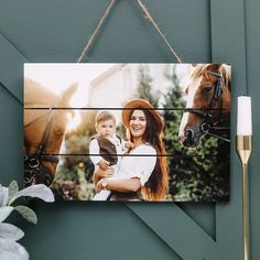 a woman holding a baby next to a horse on a wooden sign hanging from a wall