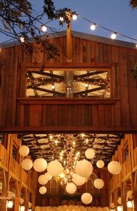 the inside of a barn with paper lanterns hanging from it's ceiling and lights on the outside