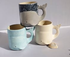 three coffee mugs with different designs on them, one has a fish and the other has a shell