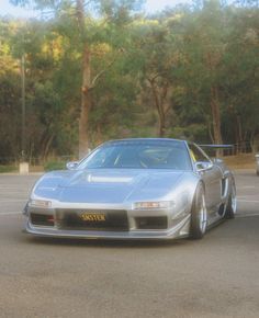 a silver sports car driving down a street next to another one in the parking lot