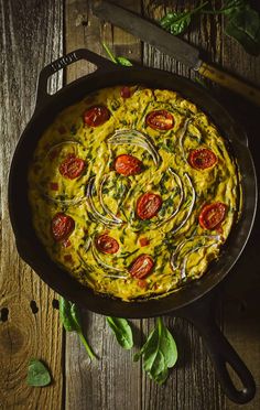 an omelet with tomatoes and spinach in a cast iron skillet on a wooden table