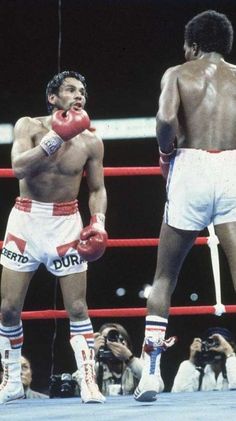 two men standing next to each other in a boxing ring, one wearing red and the other white