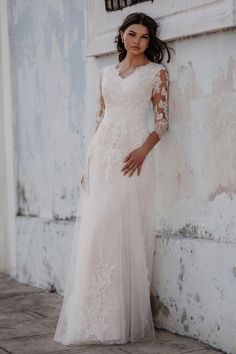 a woman standing next to a white wall wearing a dress with long sleeves and an open back