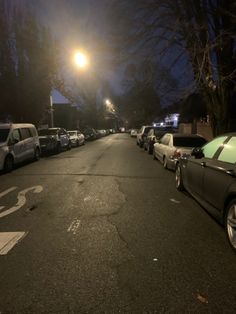 cars parked on the side of a street at night with one car driving down the road