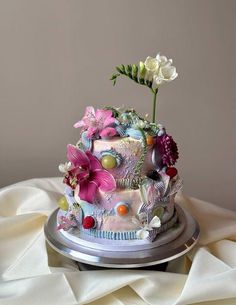 a multi - layered cake decorated with flowers on a silver platter atop a white cloth