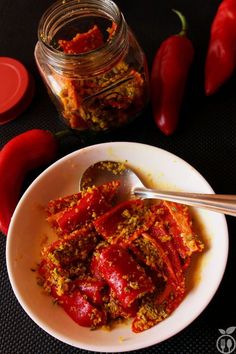 a white bowl filled with red peppers next to a jar of chili paste and two spoons