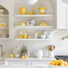 a white kitchen with yellow and white accessories on the shelves above it is also filled with lemons