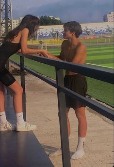 a man and woman leaning against a rail at a baseball field with the sky in the background