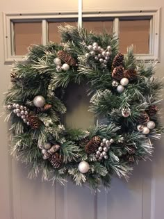 a christmas wreath hanging on the front door with silver balls and pine cones around it