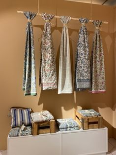 an assortment of scarves hanging from hooks in a room with tile flooring and beige walls